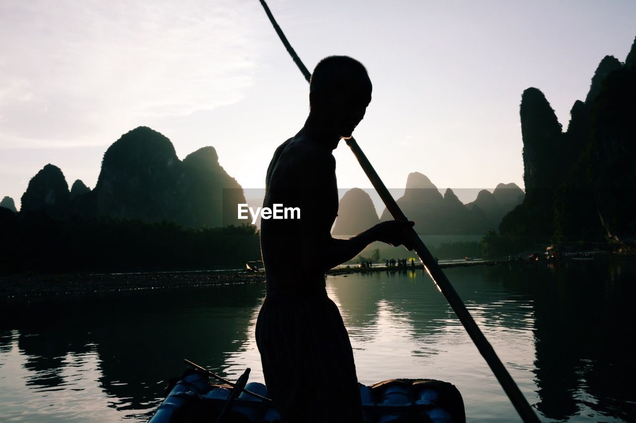 SILHOUETTE WOMAN STANDING IN LAKE AGAINST SKY