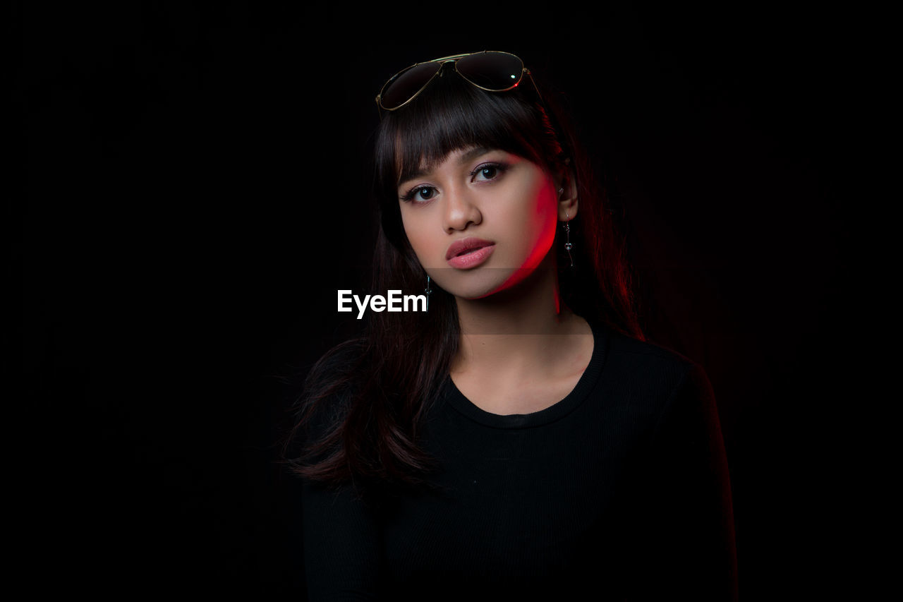 Portrait of young woman wearing sunglasses standing against black background