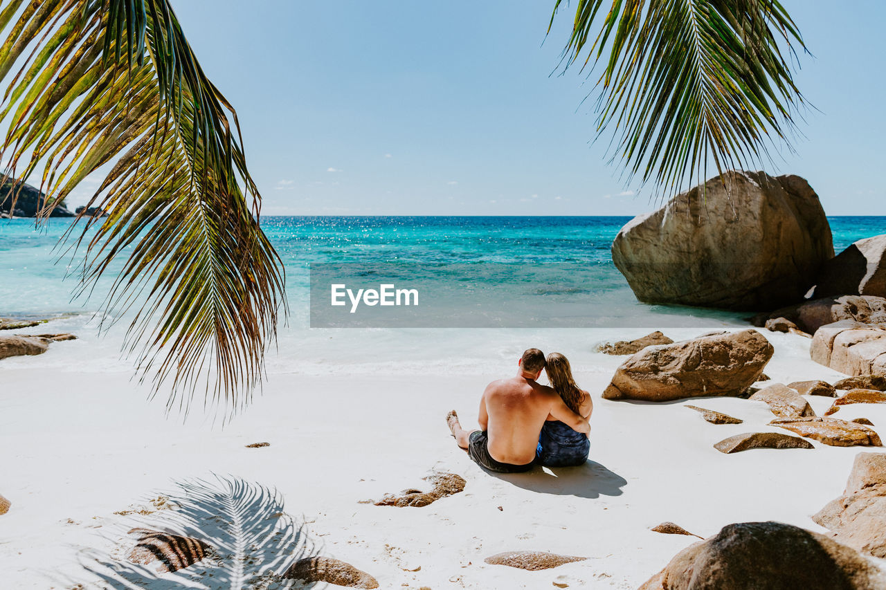 Rear view of couple sitting at beach against sky