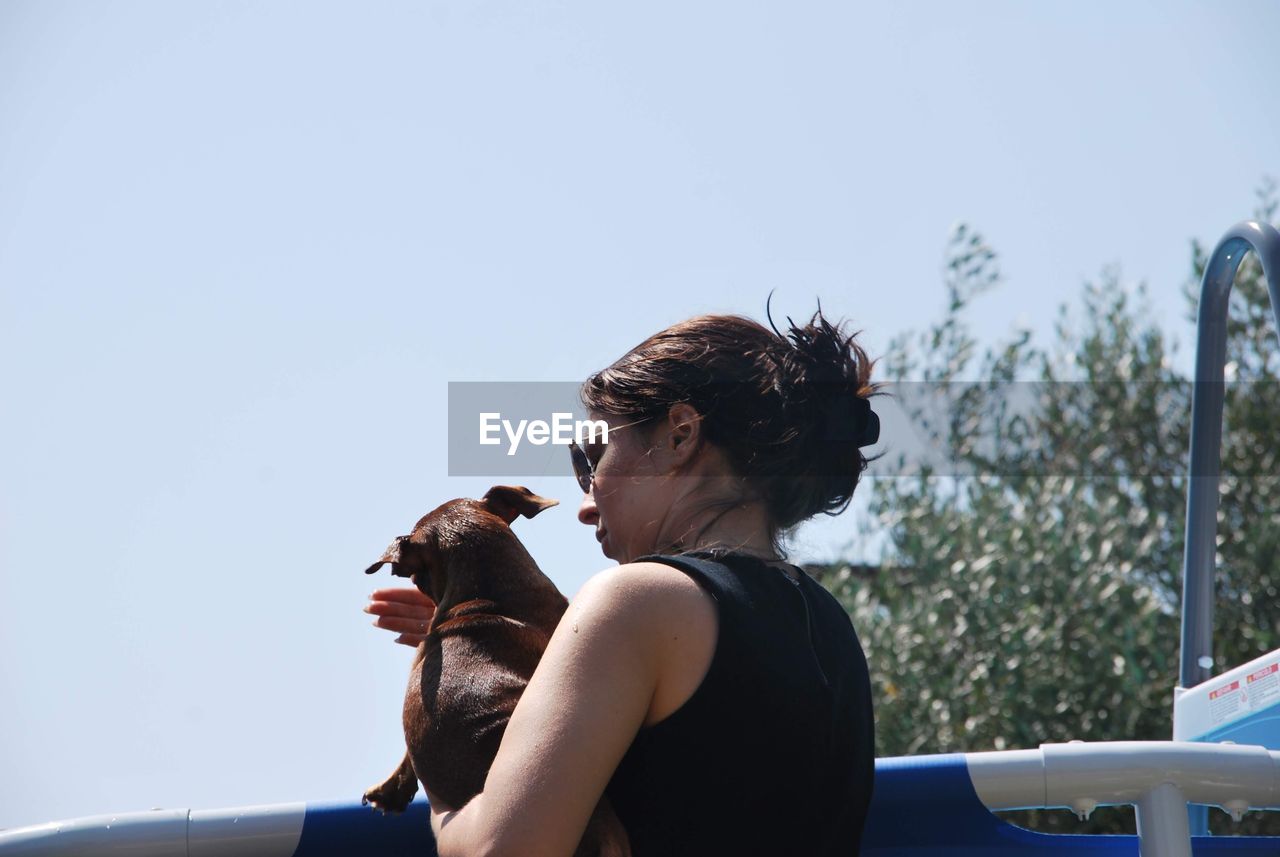 Low angle view of woman holding dog against clear sky