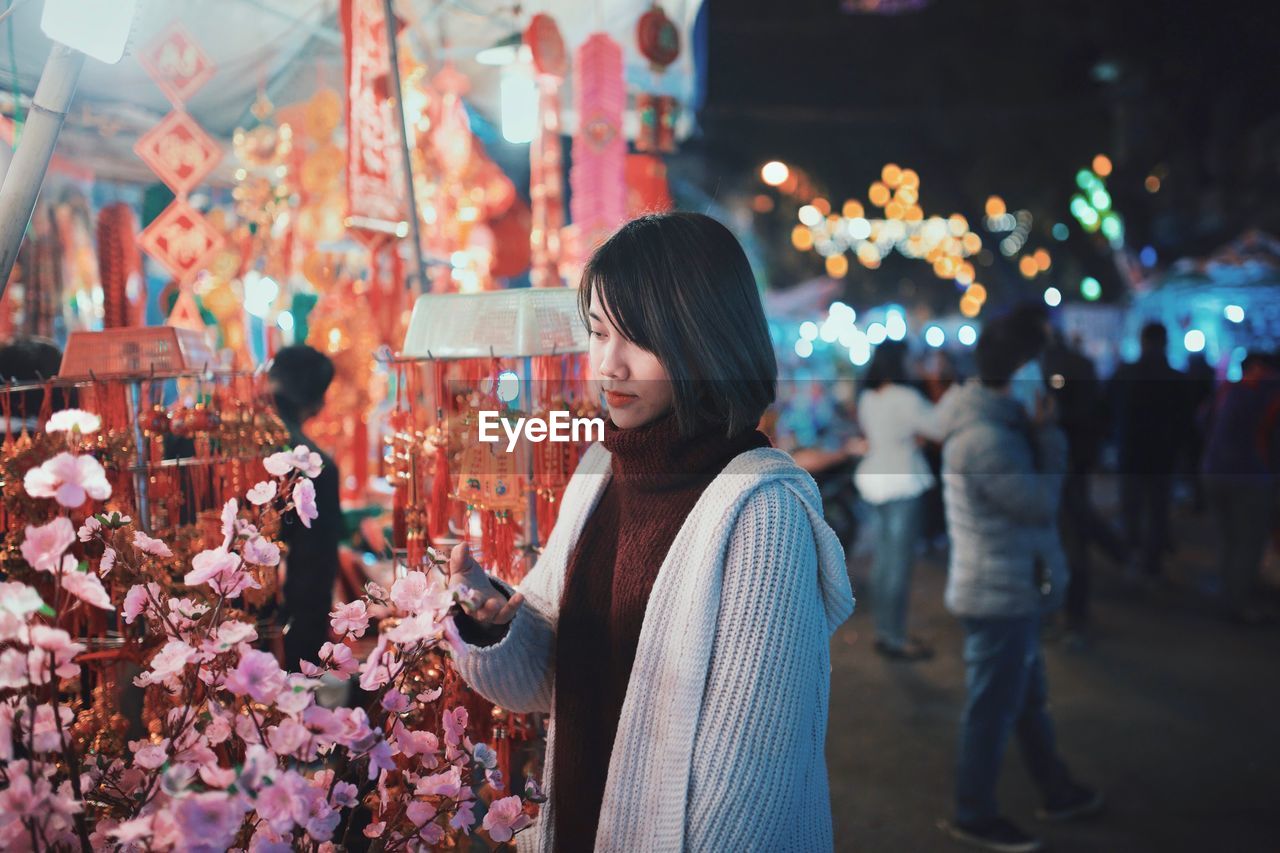 Young woman touching flowers in market at night