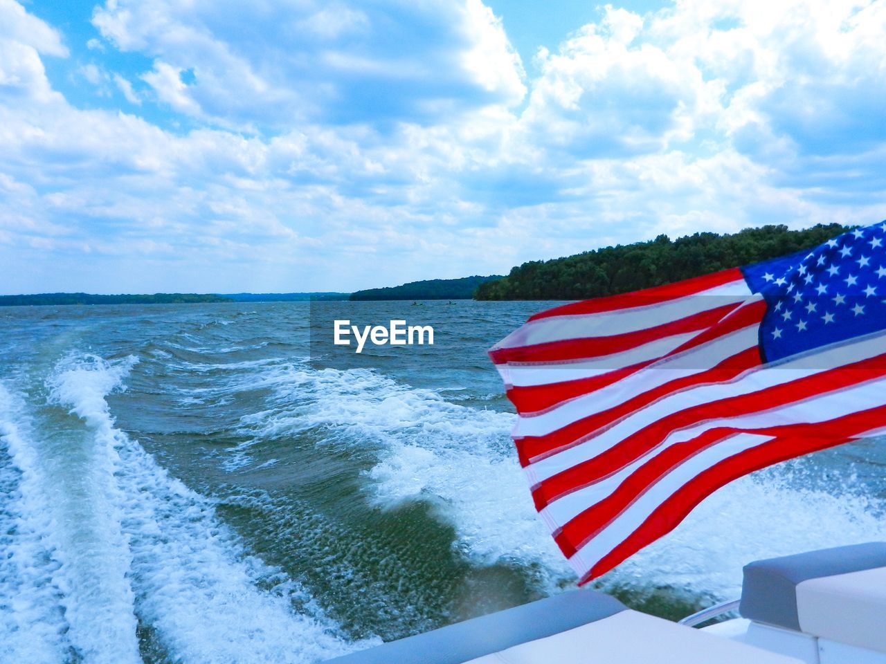 Scenic view of lake against sky from the back of a moving boat with the american flag waving in wind