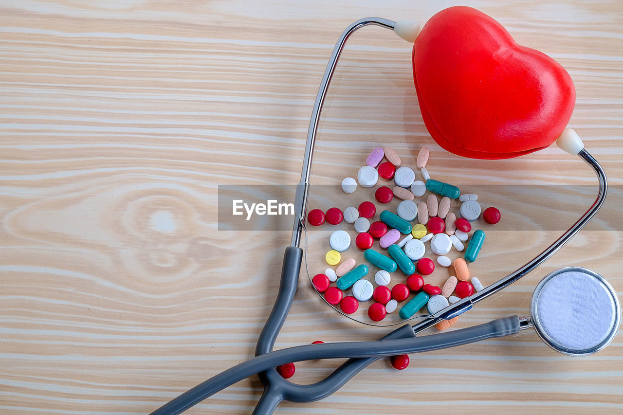 High angle view of multi colored pills with stethoscope and heart shape on table