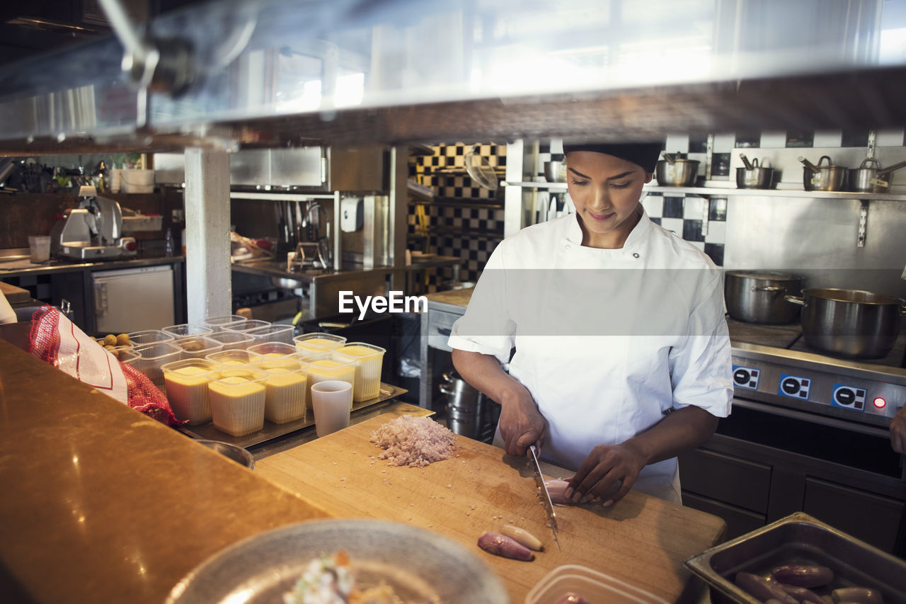 Female chef chopping onion on cutting board in kitchen at restaurant