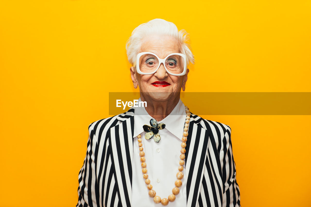 Portrait of stylish senior woman standing against yellow background