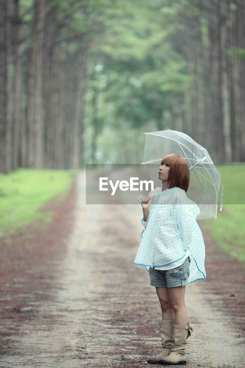 Side view of woman with umbrella standing on road against trees in forest