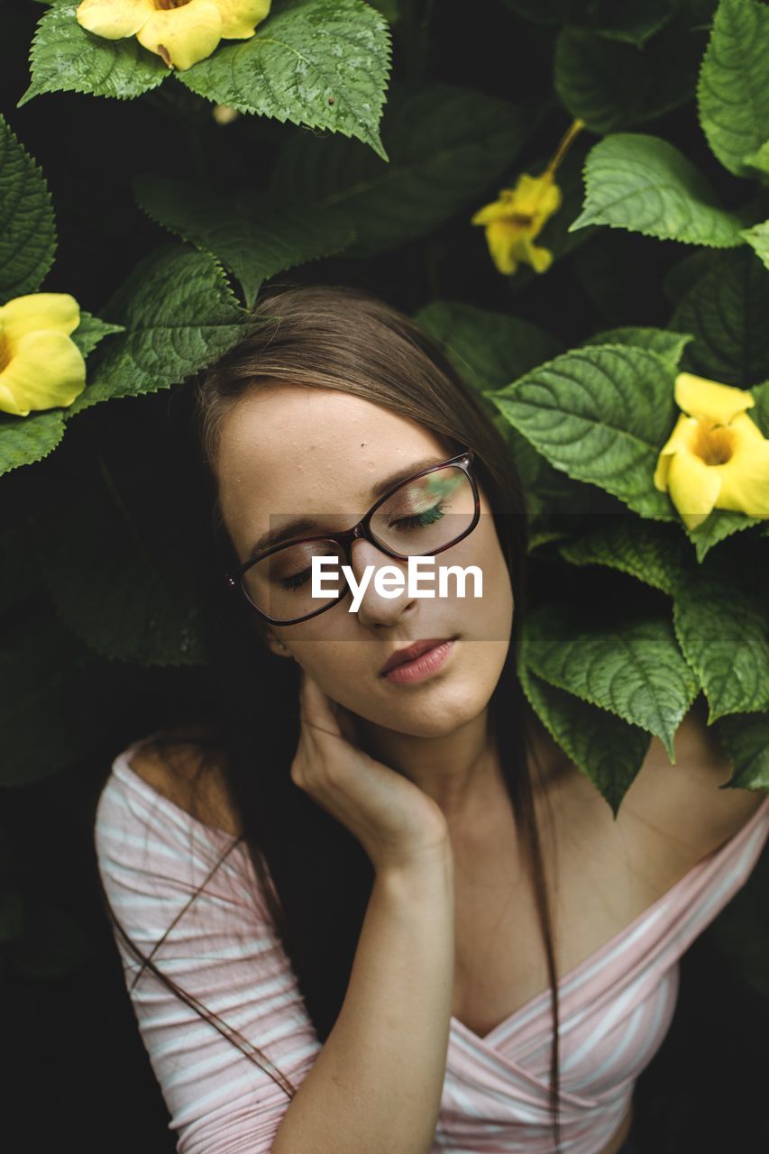 Young woman with eyes closed wearing eyeglasses by flowering plants