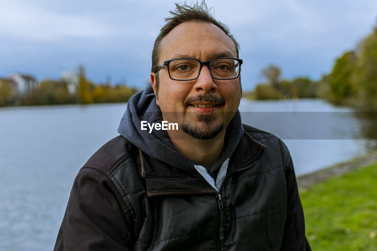 Portrait of man wearing eyeglasses standing against lake
