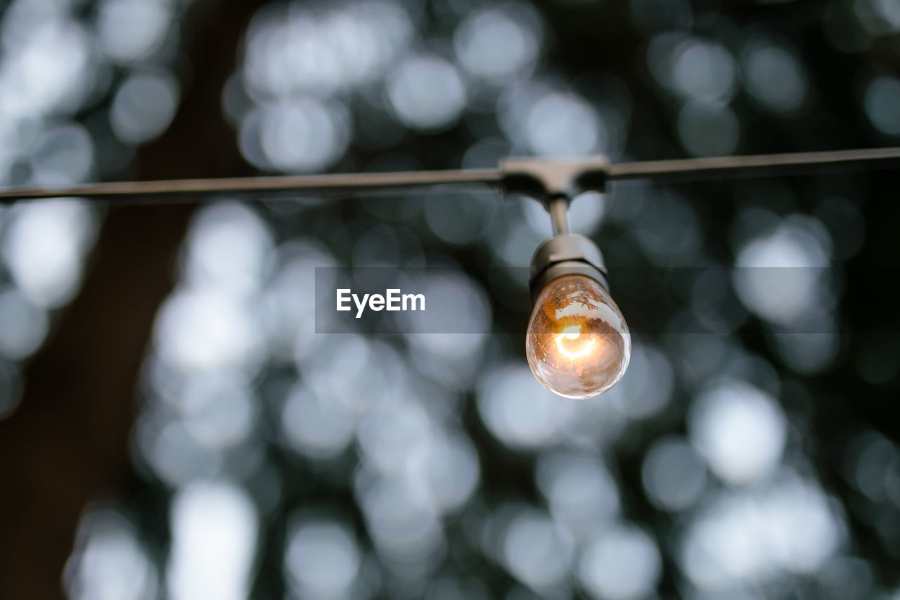 Low angle view of illuminated light bulb hanging outdoors