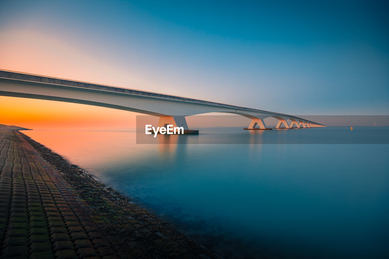 VIEW OF BRIDGE OVER SEA AGAINST SKY DURING SUNSET