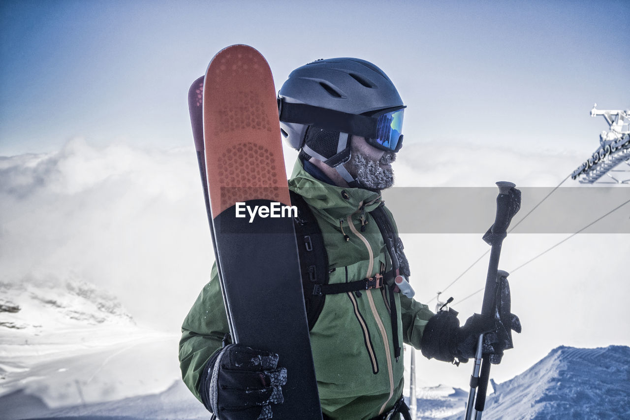 Man with skis standing on snow covered mountain