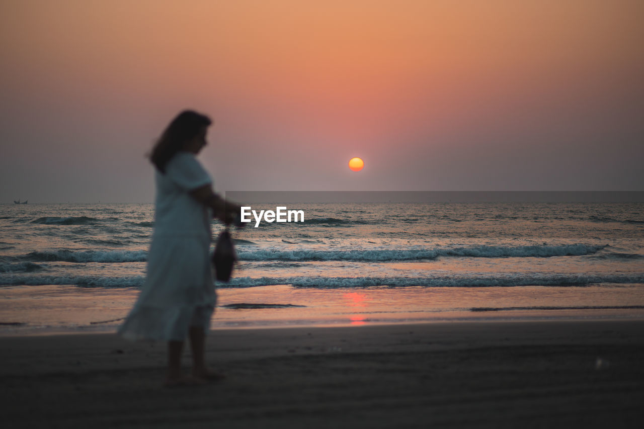 Silhouette of woman standing at beach during sunset