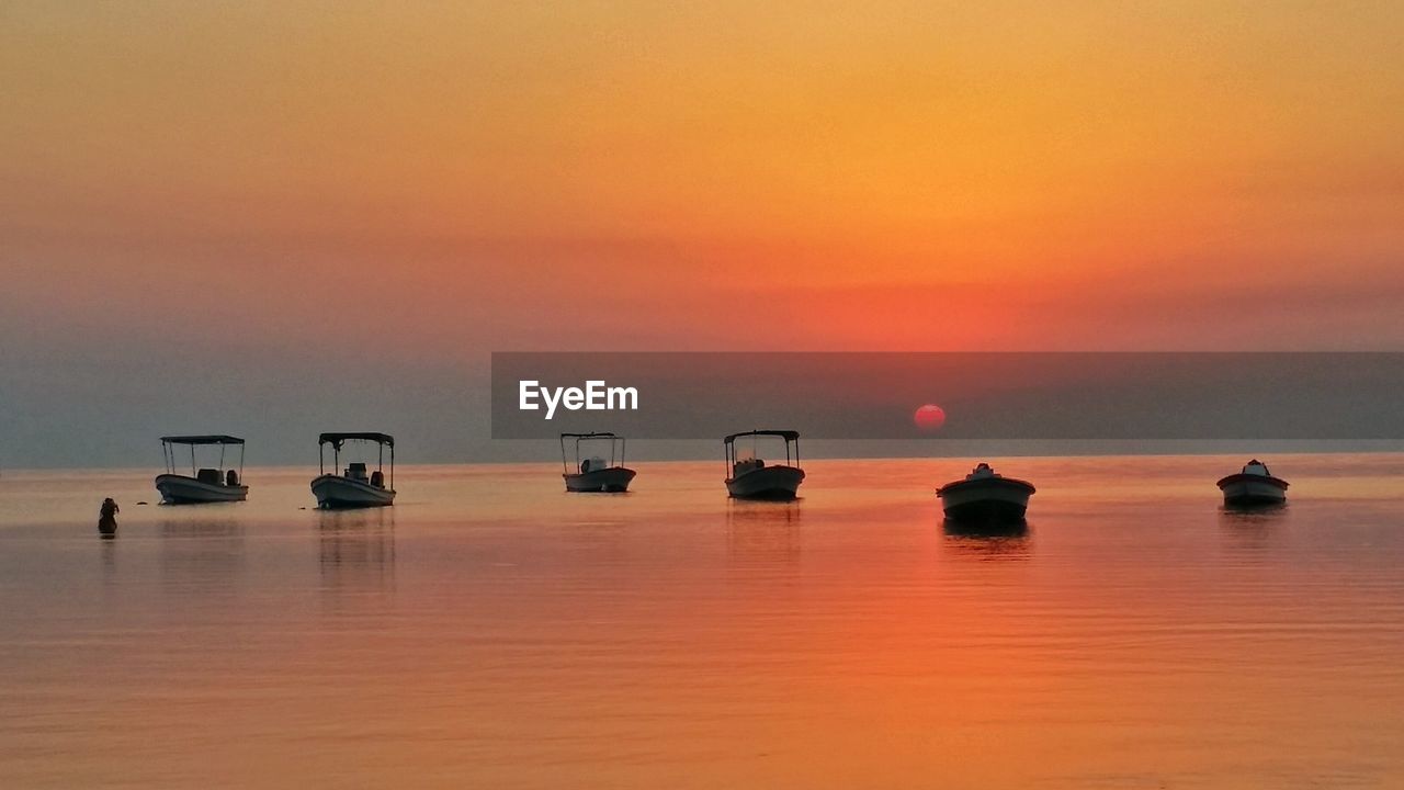 Boats in calm sea at sunset