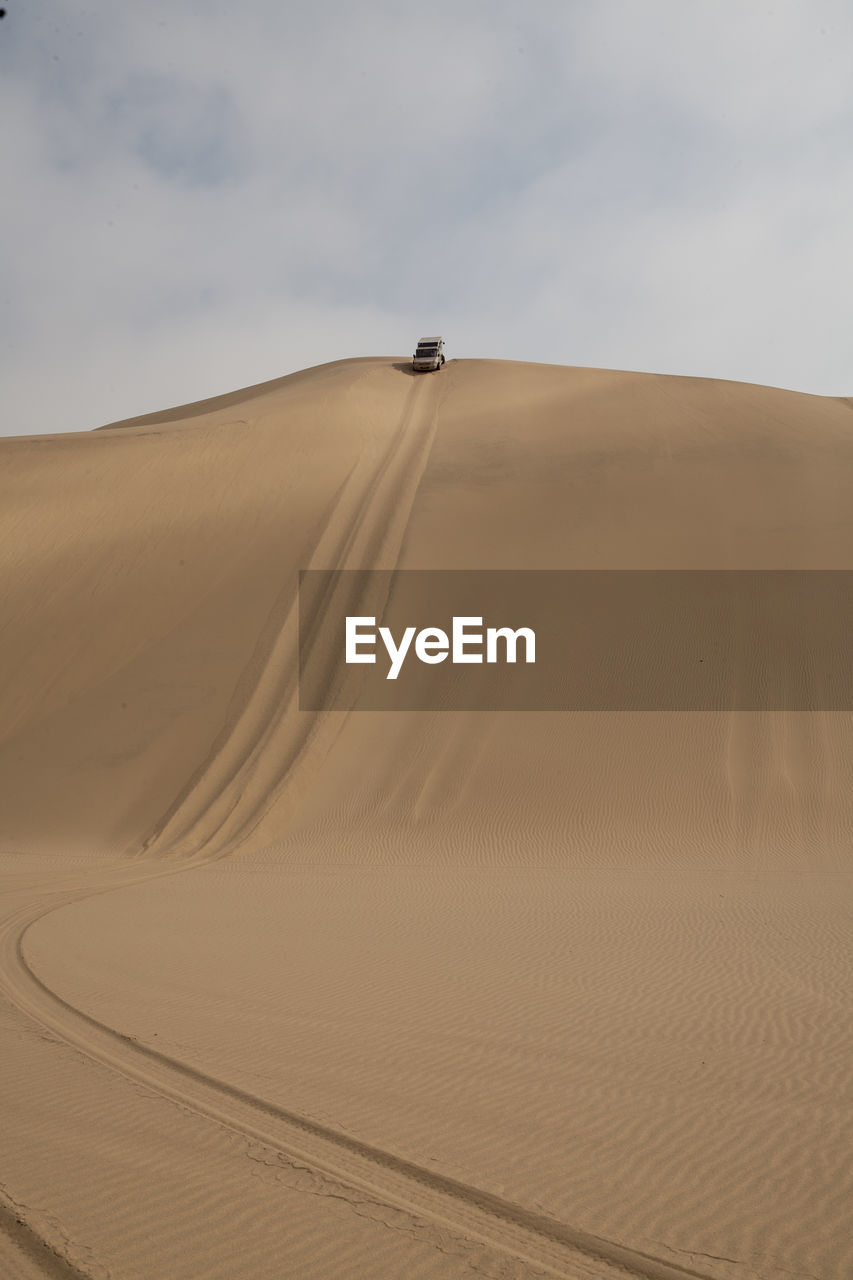 Distant view of off-road vehicle moving down sand dune against sky