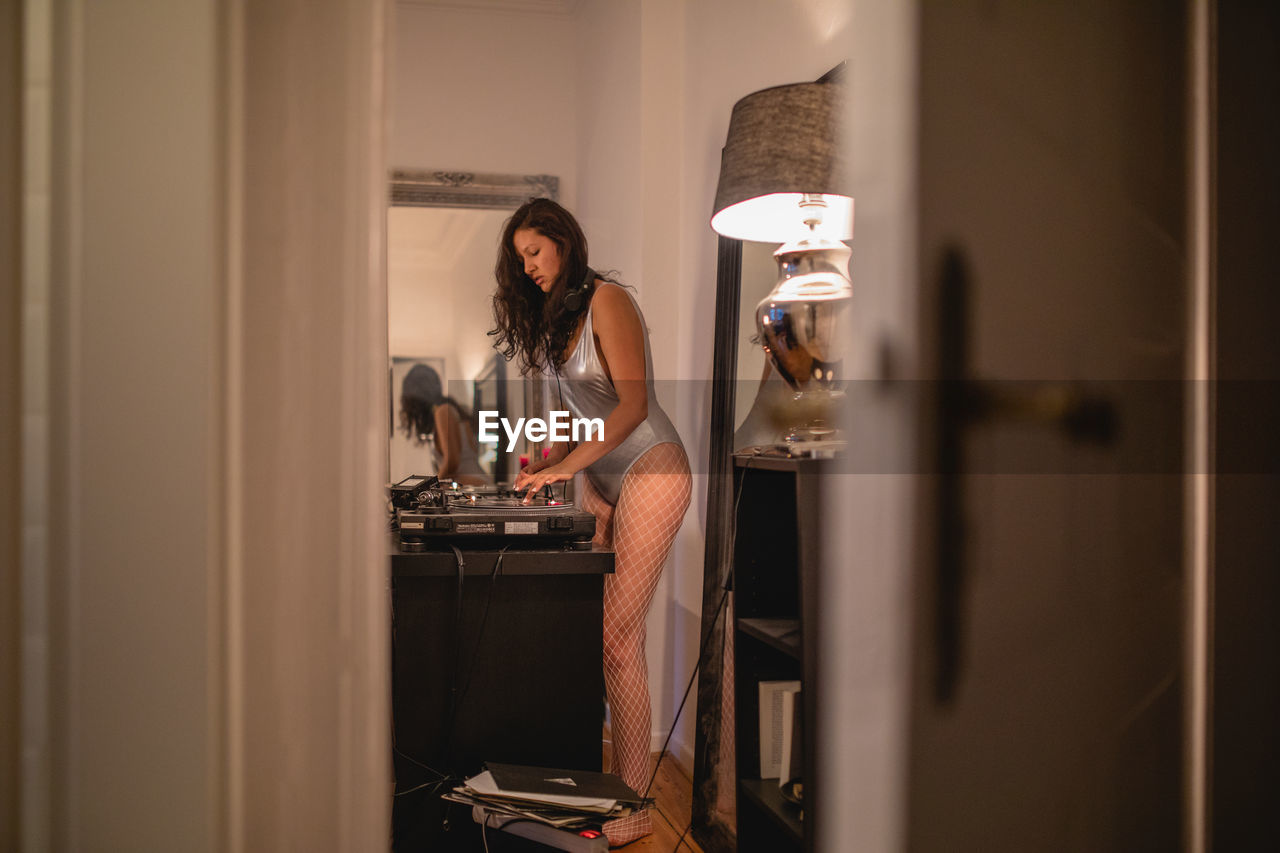 WOMAN STANDING BY WINDOW AT HOME AT NIGHT