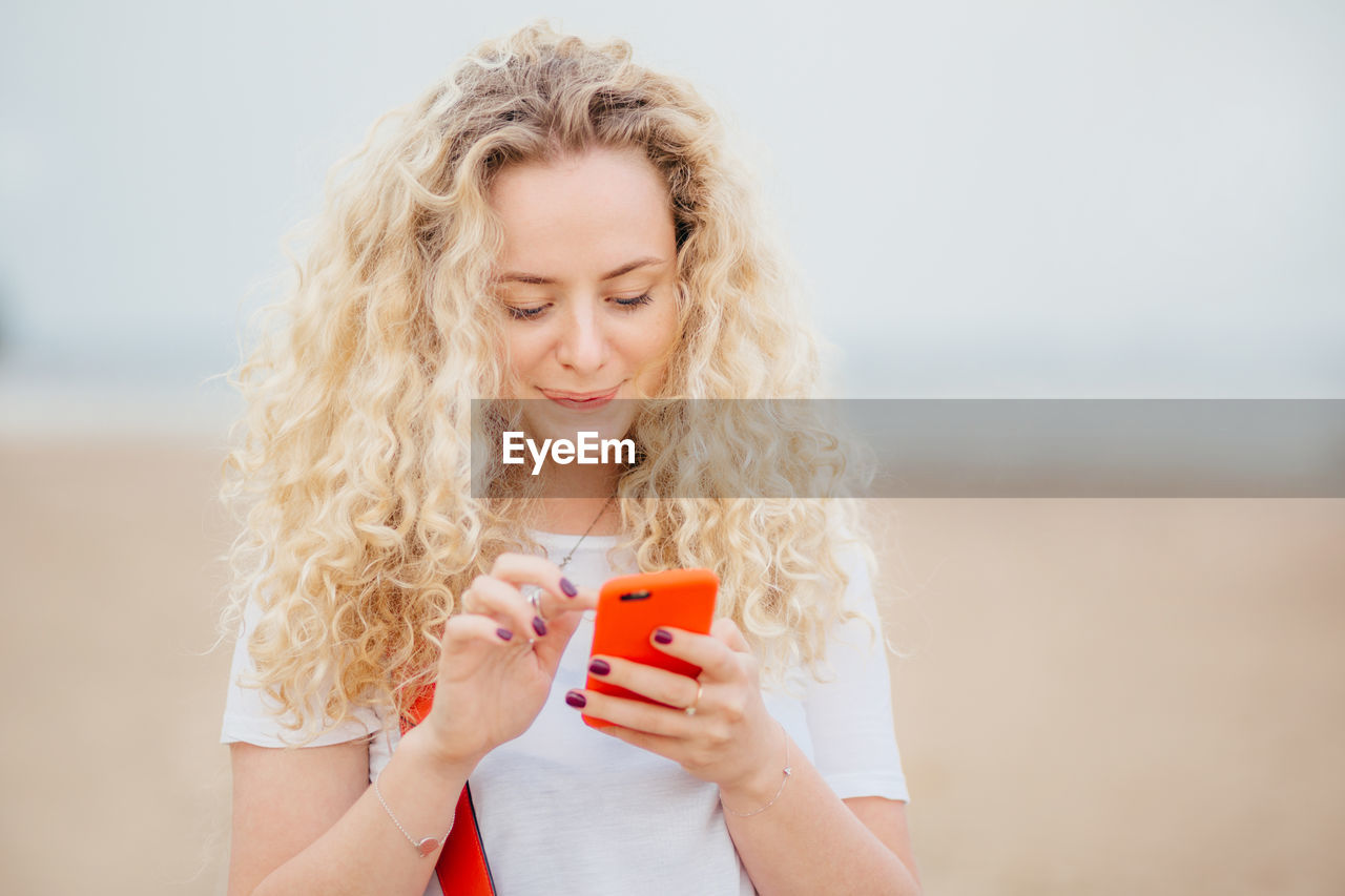 CLOSE-UP OF YOUNG WOMAN USING MOBILE PHONE WHILE HOLDING SMART