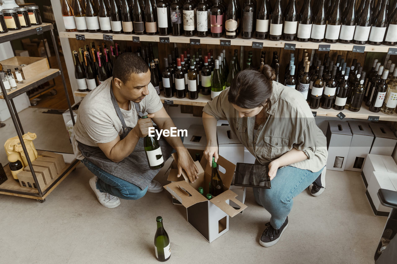 Male and female business owners removing bottles from box at wine store