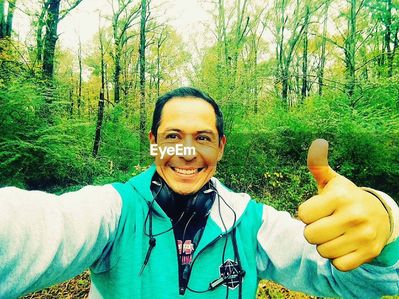 PORTRAIT OF A SMILING YOUNG MAN WEARING MASK AGAINST TREES