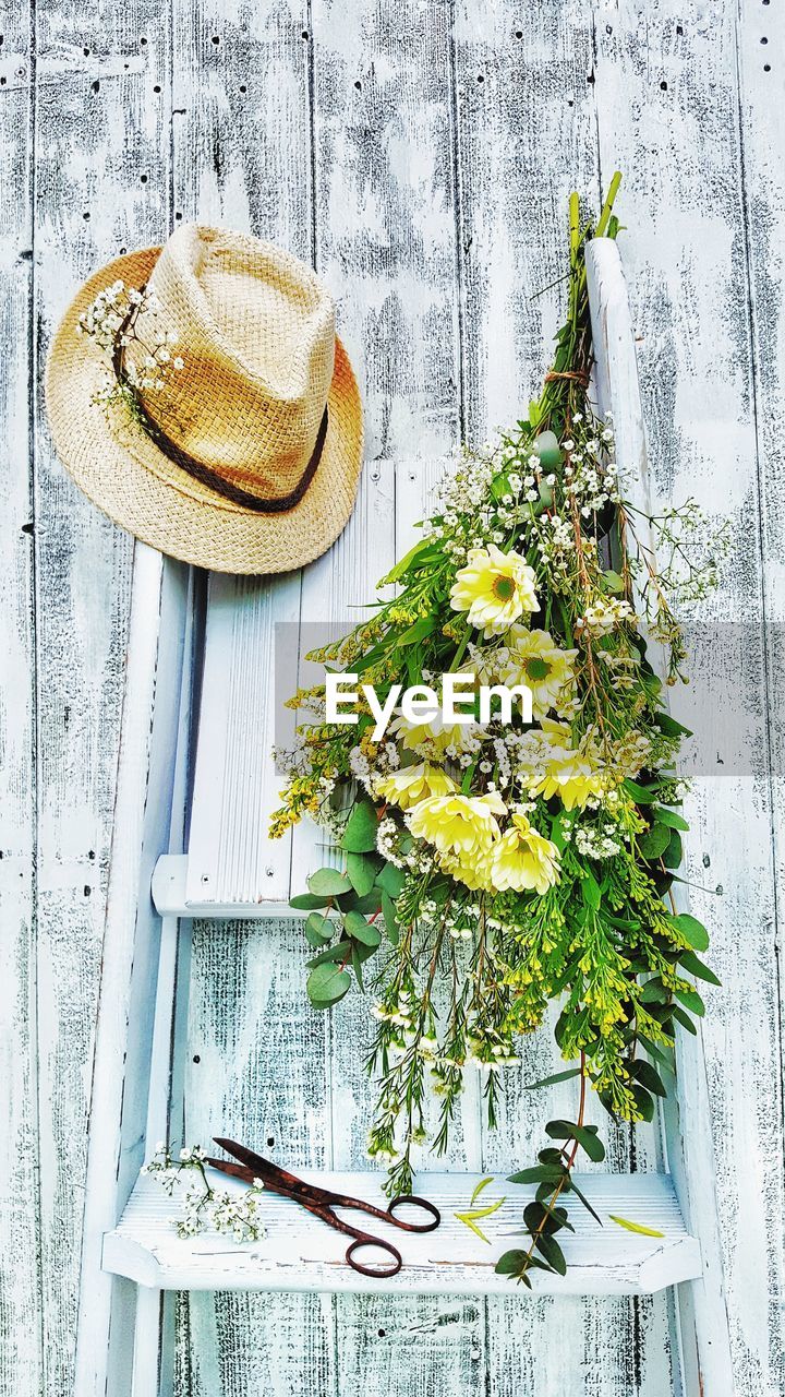 Flowers and hat on ladder against wooden wall