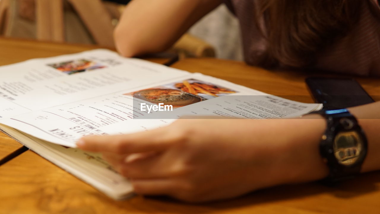 Cropped image of woman with menu at table in restaurant