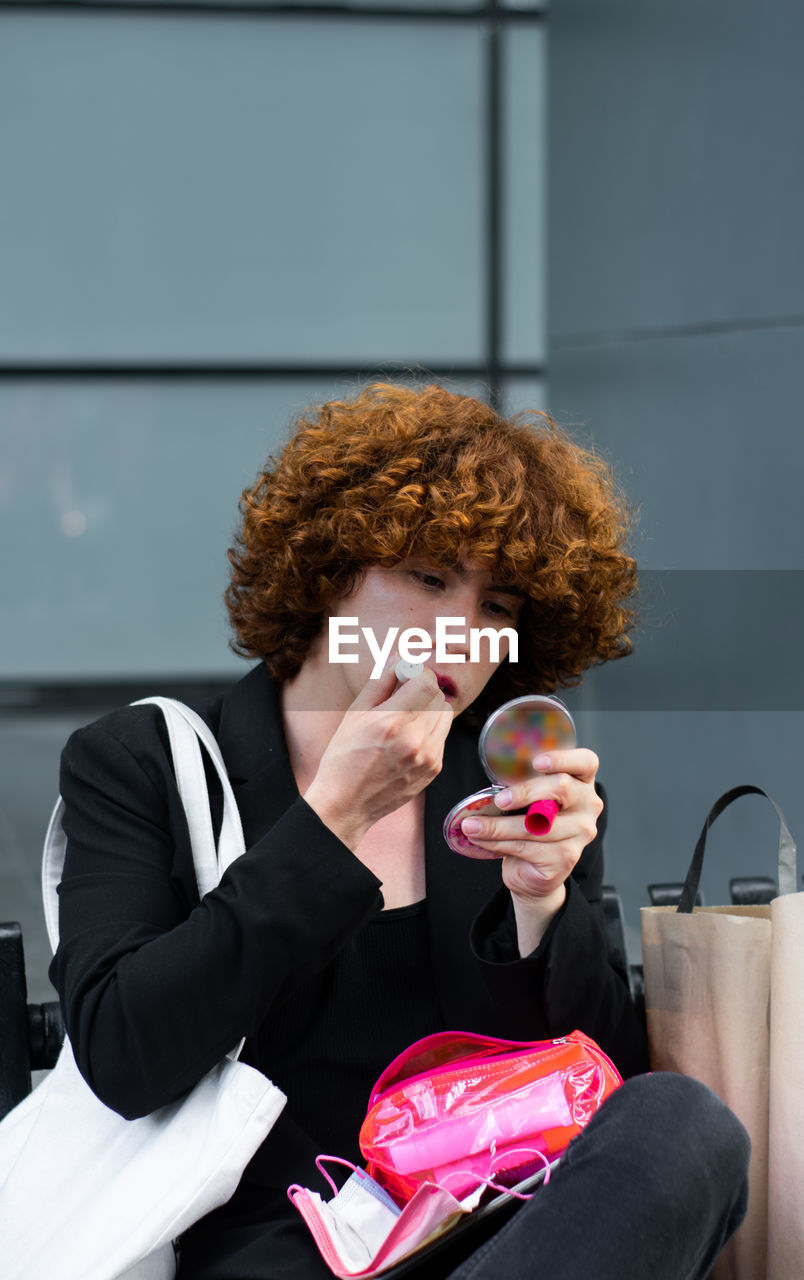 A non-binary person applies makeup sitting on a bench