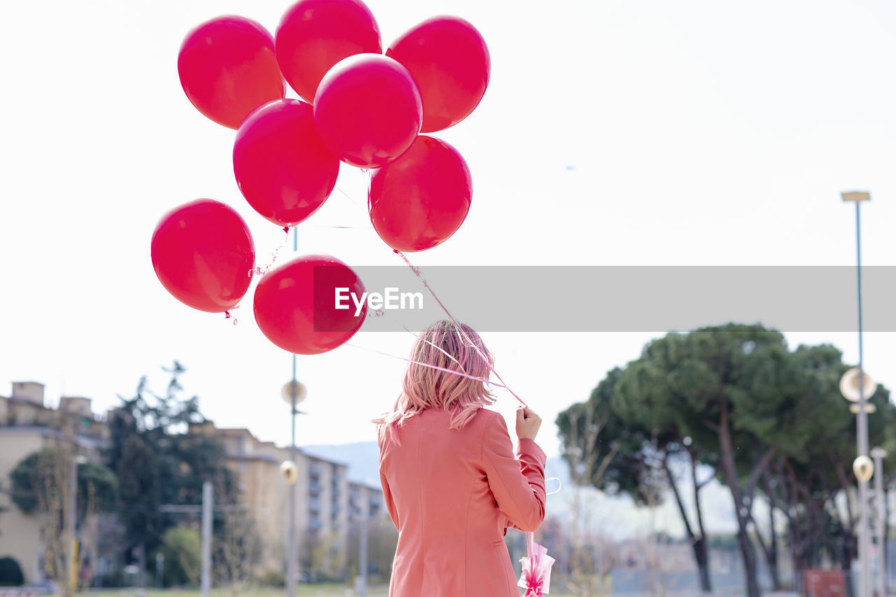 Woman in smart casual holding bunch of pink balloons