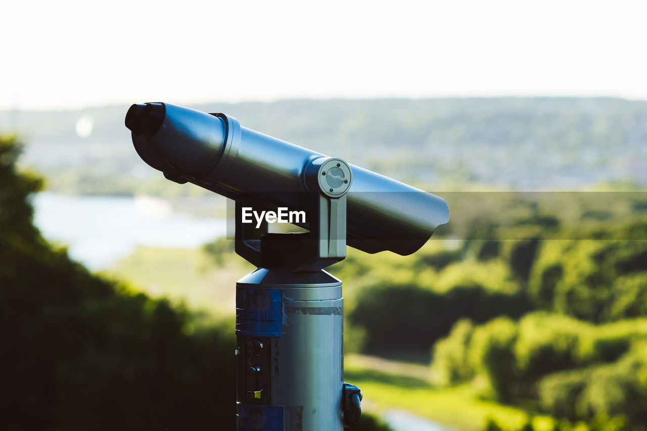 CLOSE-UP OF COIN-OPERATED BINOCULARS AGAINST SKY ON FIELD