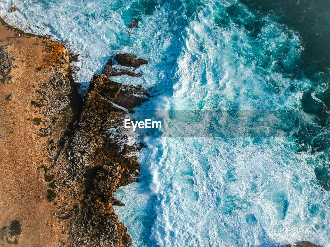 Aerial top view of sea waves hitting rocks on the beach with turquoise