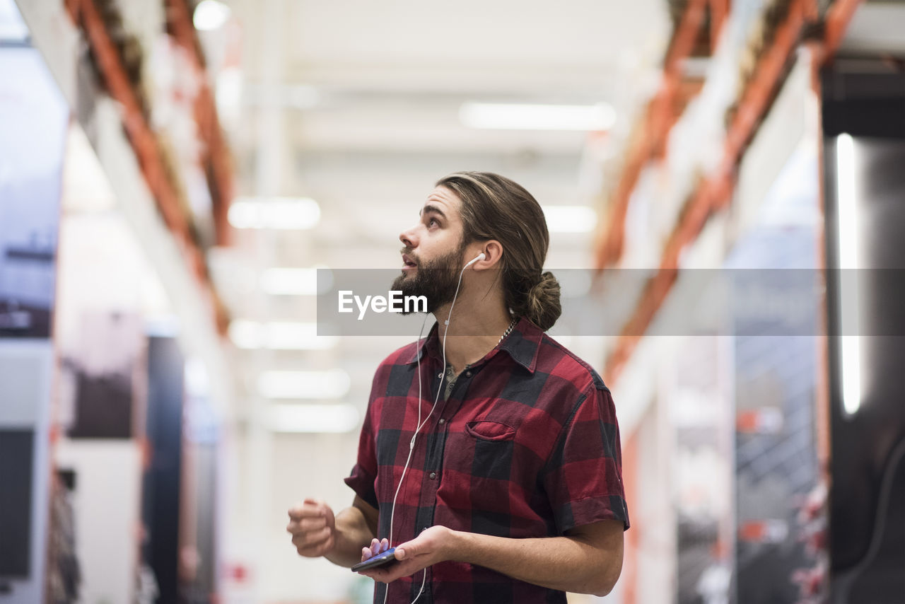 Customer looking up while listening music through smart phone at hardware store