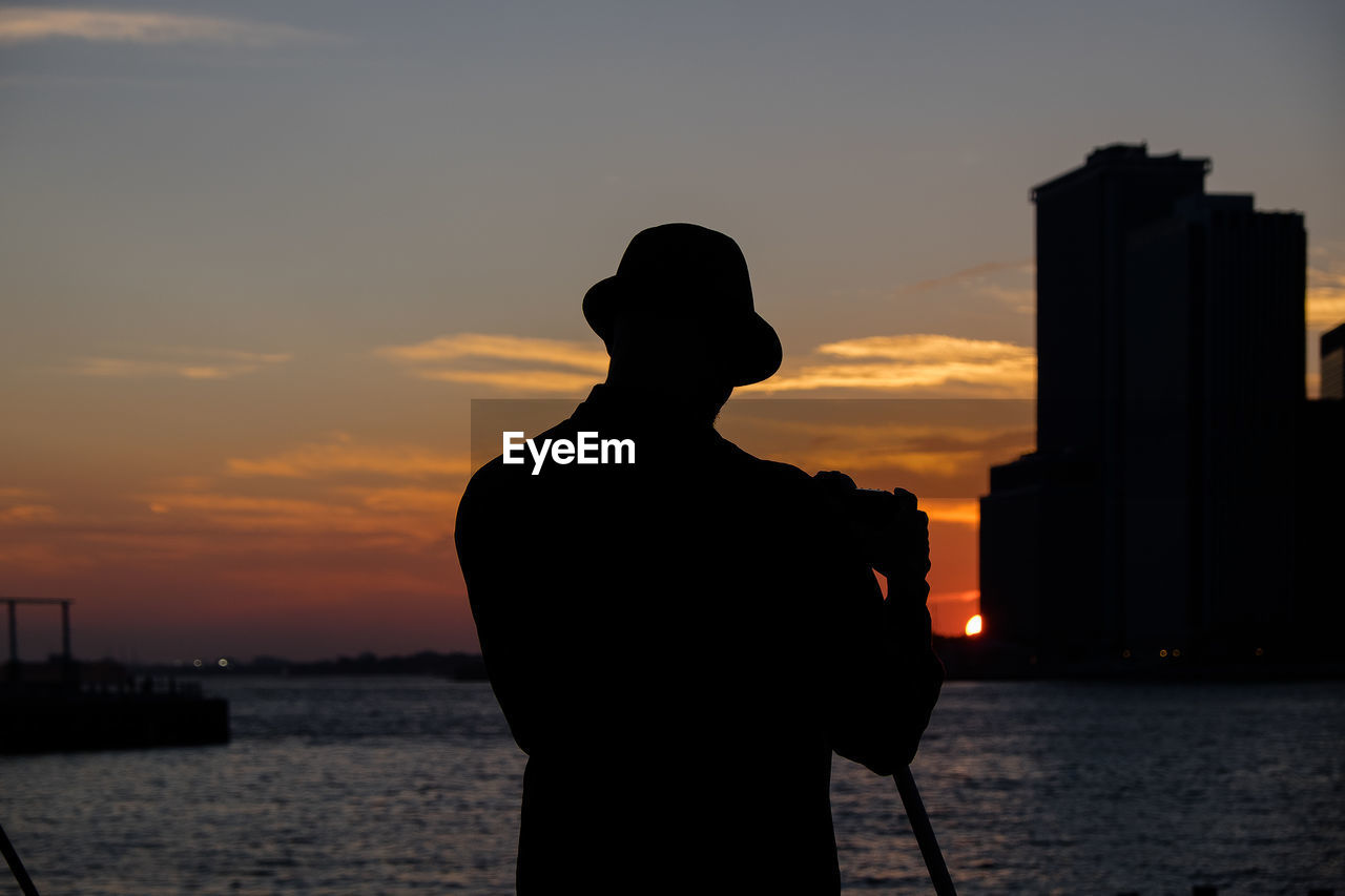 Rear view of man standing against sea during sunset