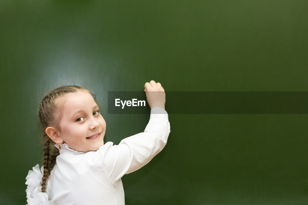 Portrait of smiling girl standing against blackboard
