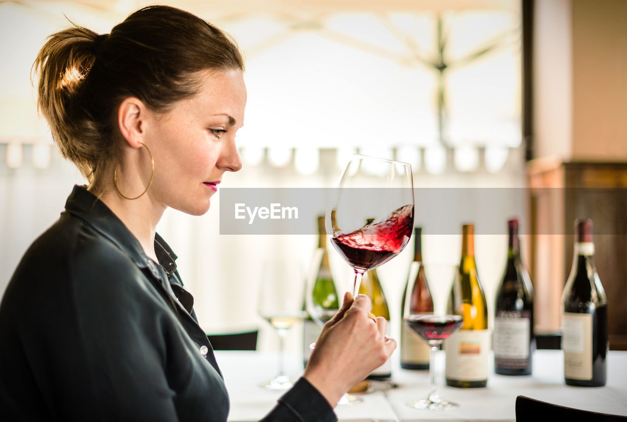 Side view of woman shaking red wine in wineglass