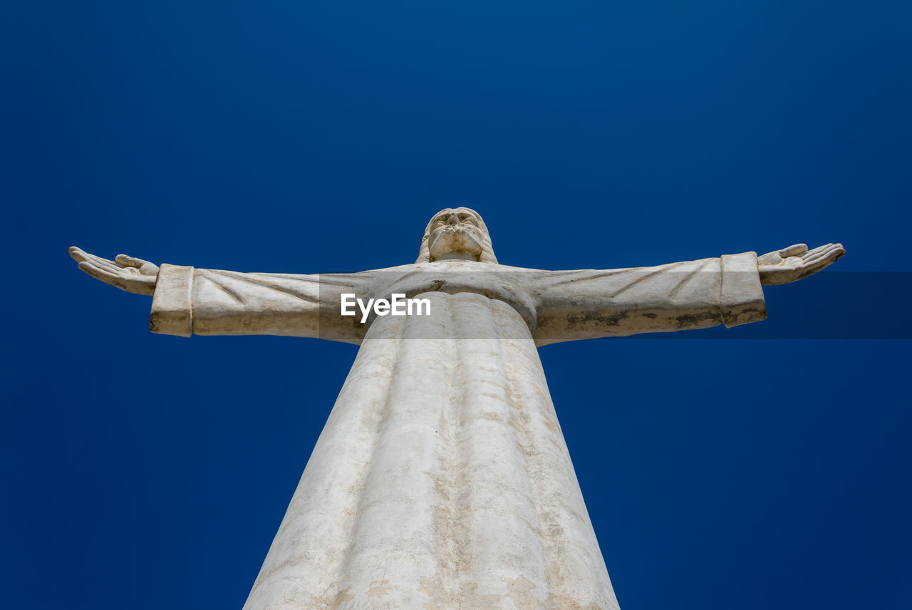 Low angle view of jesus christ statue against blue sky, lubango, angola