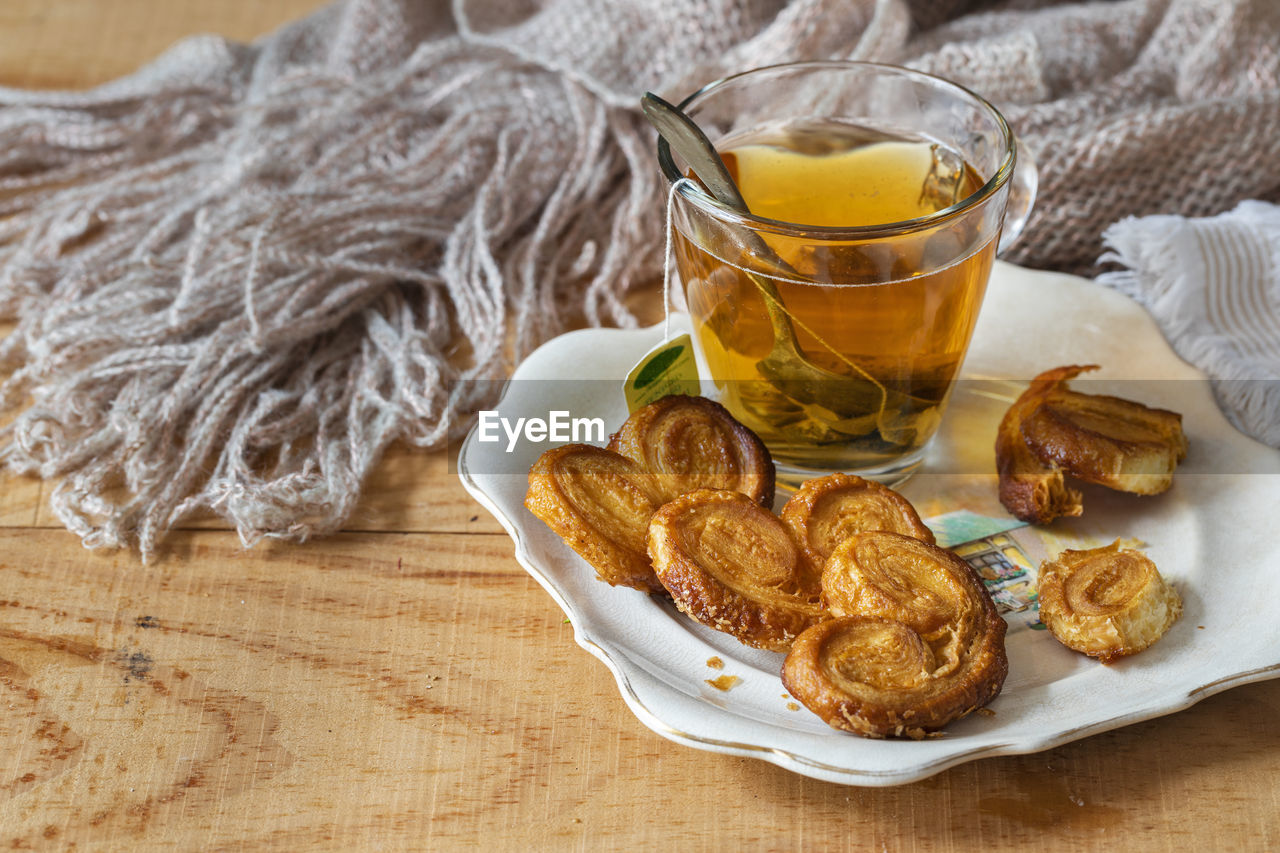 A cup of tea on a saucer with some puff pastries. behind a soft wool scarf with fringes.