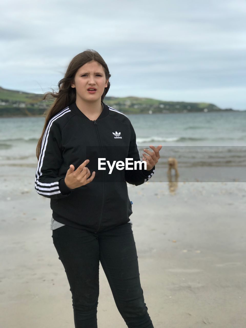 PORTRAIT OF TEENAGE GIRL STANDING ON BEACH