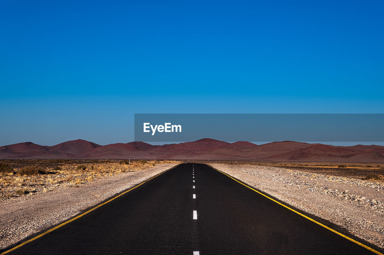 ROAD LEADING TOWARDS DESERT AGAINST BLUE SKY