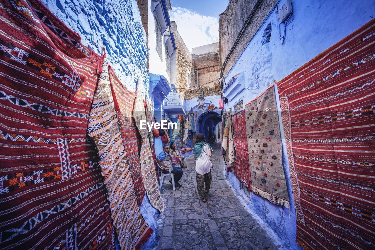 REAR VIEW OF PEOPLE WALKING AGAINST BUILDING