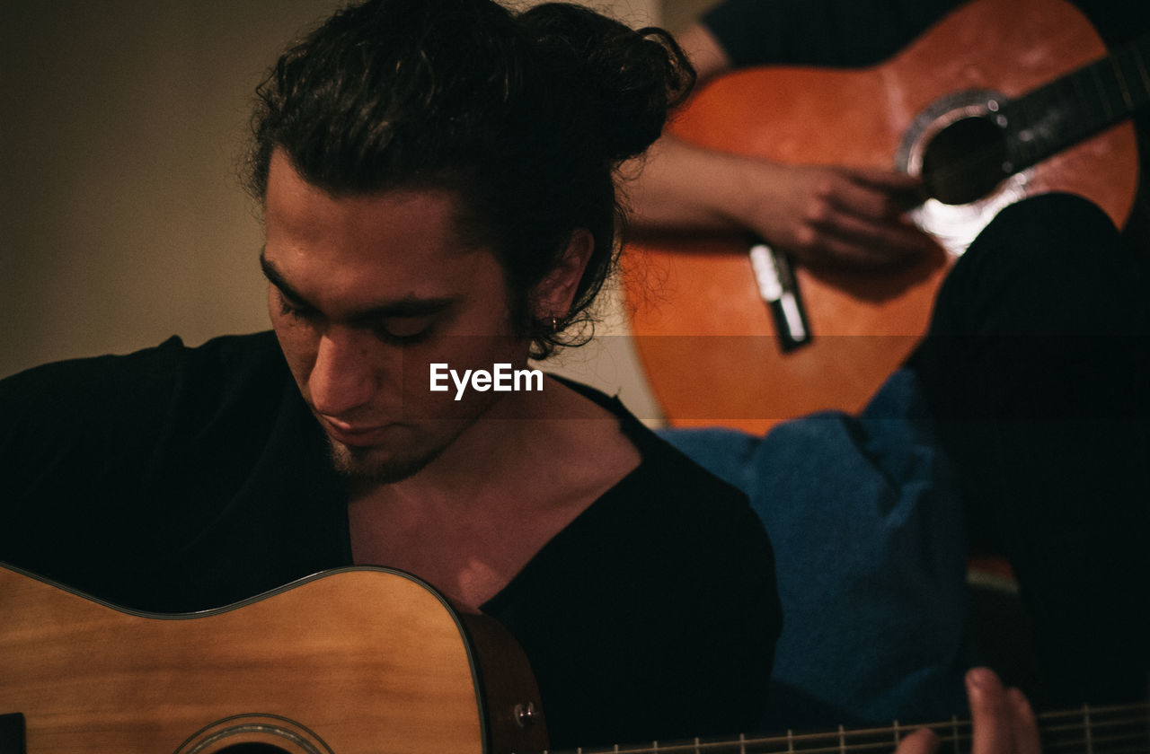 Young man playing guitar with friend at home