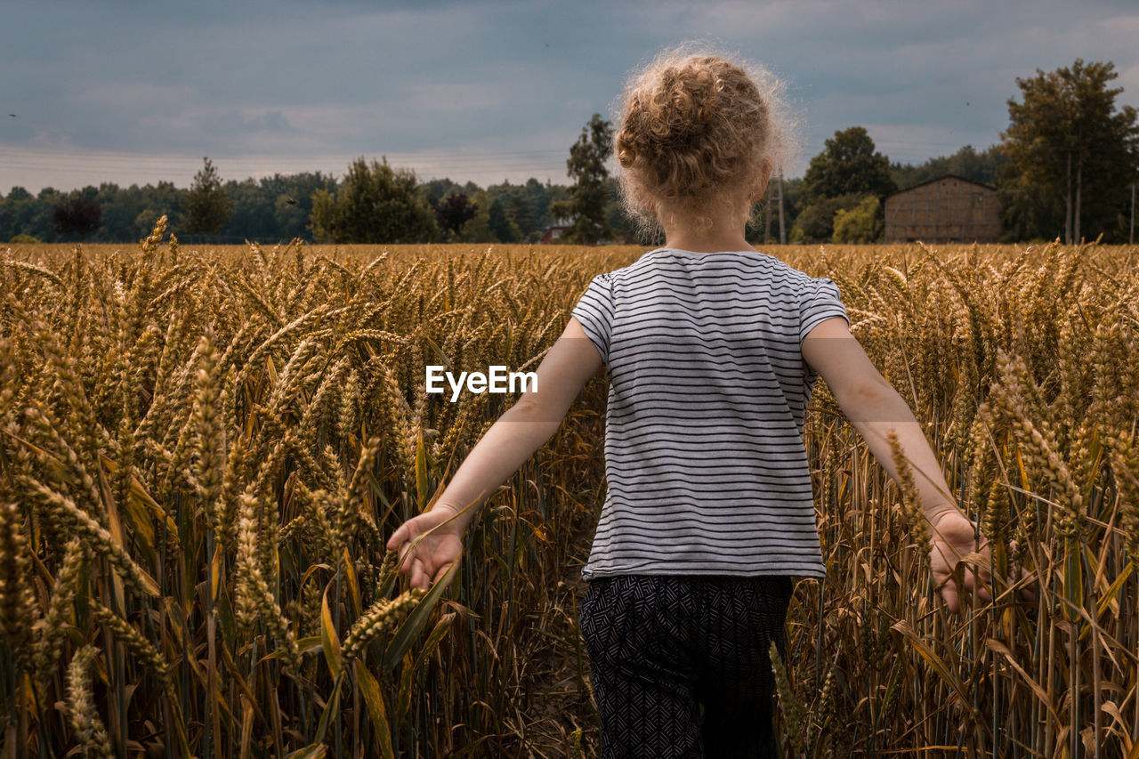 Rear view of girl standing on wheat field