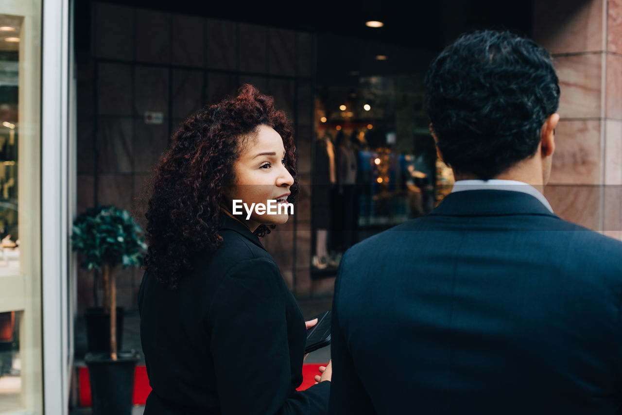 Rear view of businesswoman talking with businessman while walking against building in city