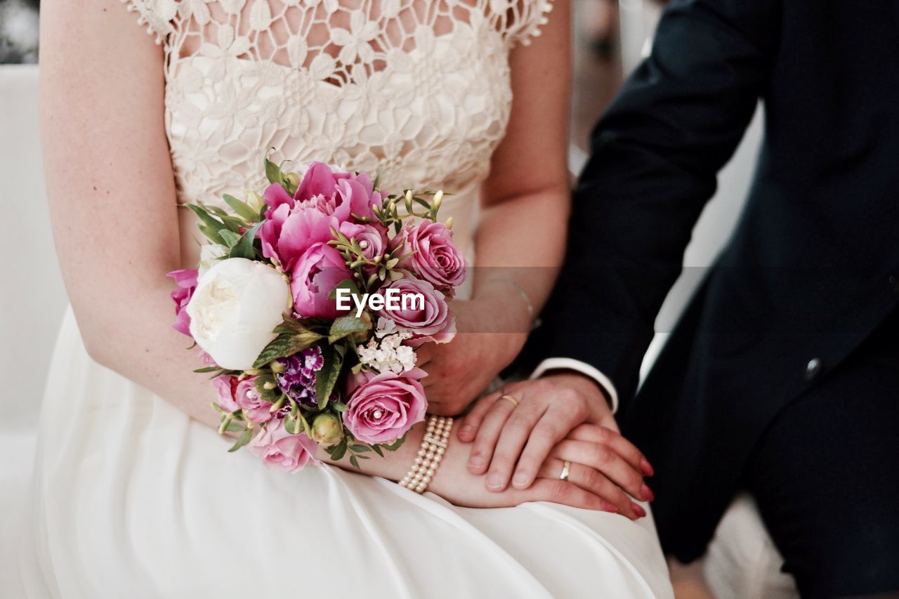 Midsection of bride holding flower bouquet while holding hand of husband