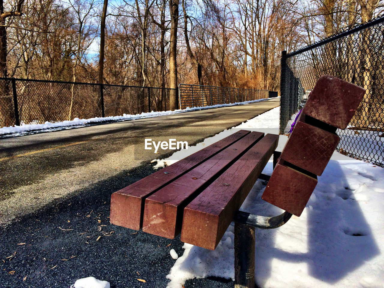 Empty bench on snow covered footpath