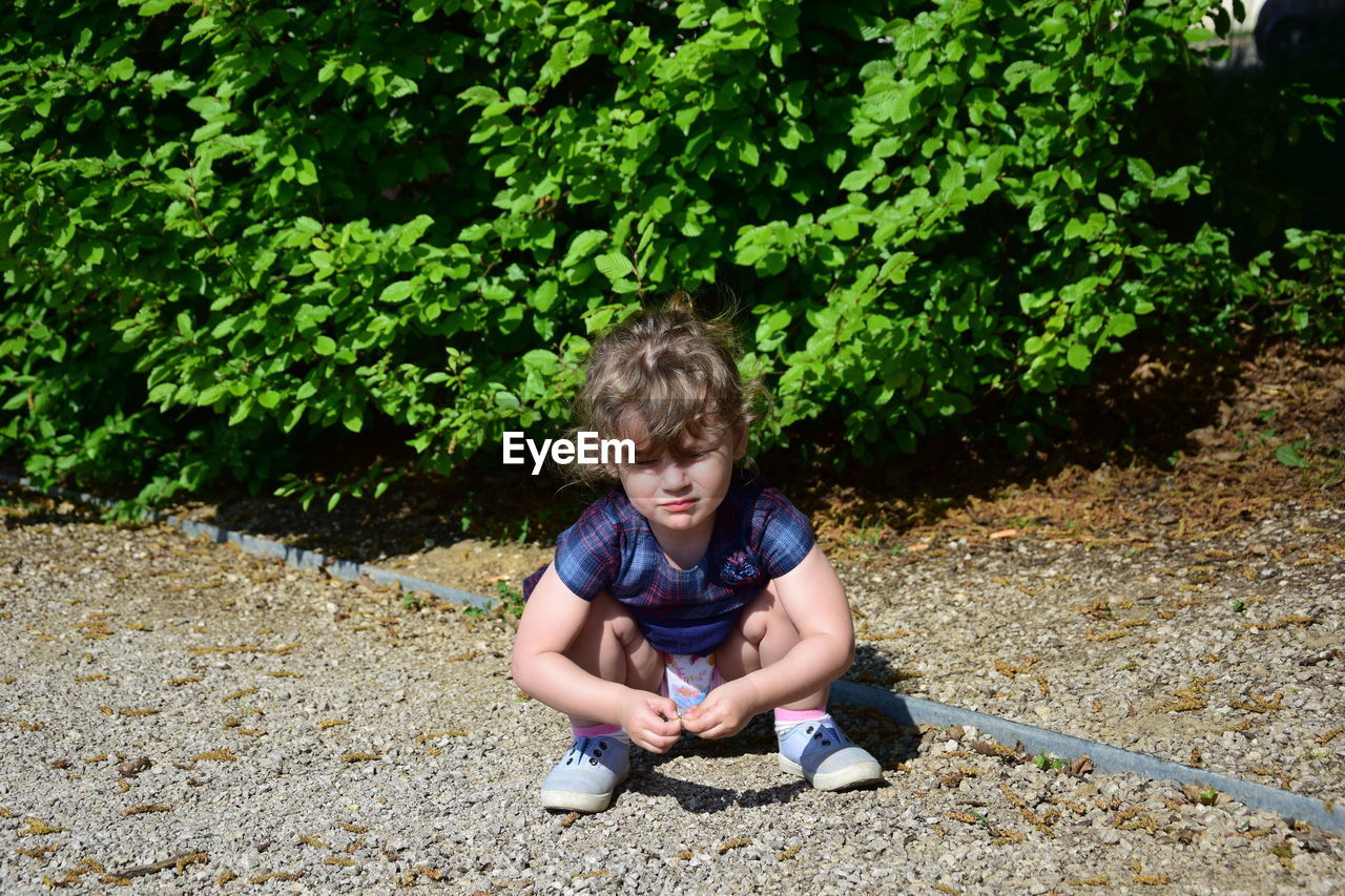 Full length of girl crouching on footpath against plants