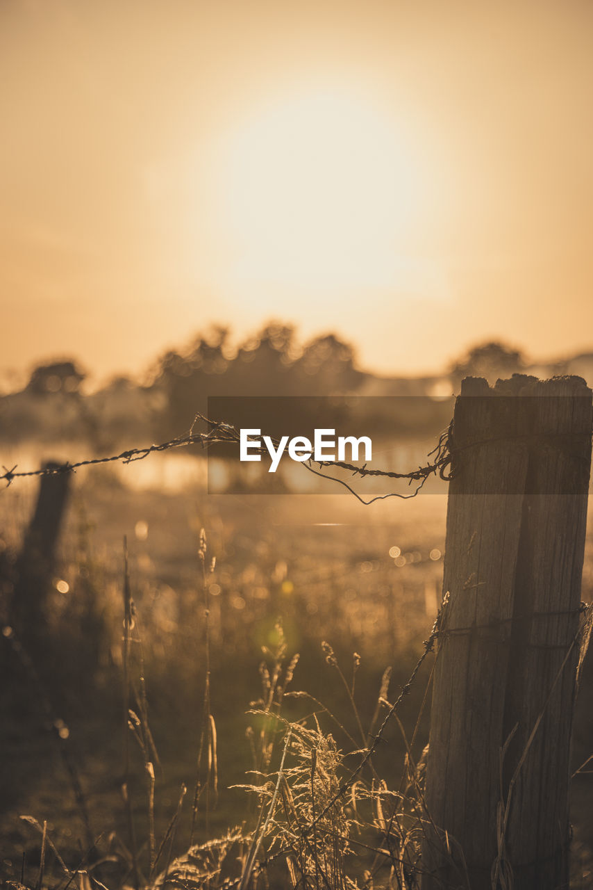 Barbed wire fence on field against sky during sunset