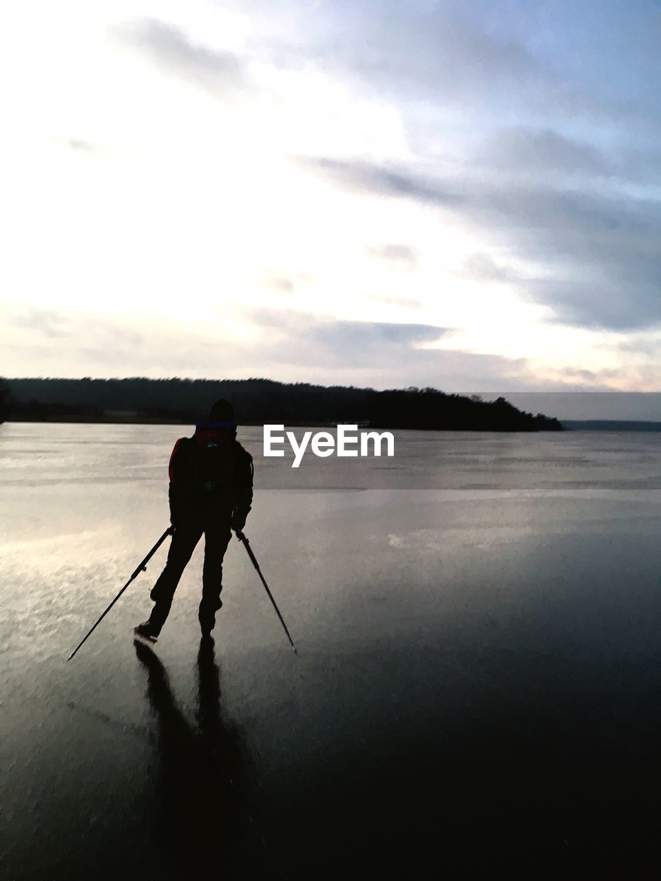 Silhouette man standing on ice rink against sky