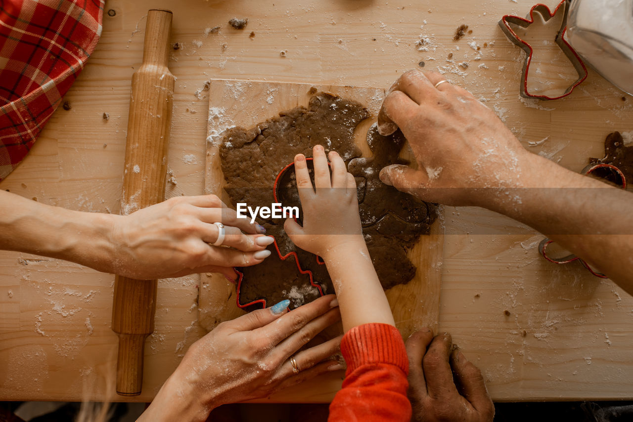 Top view of kid's and parents hands making christmas cookies or ginger bread in cozy kitchen 