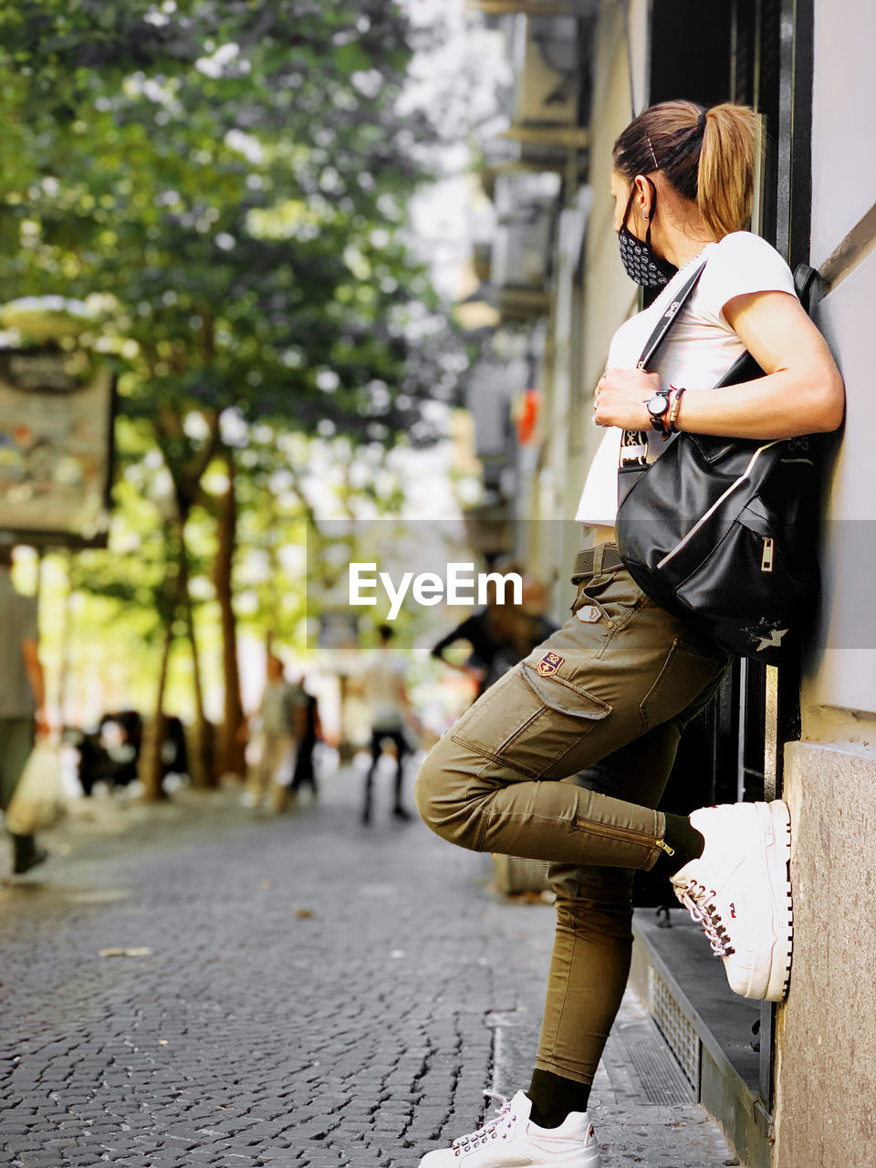 YOUNG WOMAN STANDING ON FOOTPATH IN CITY