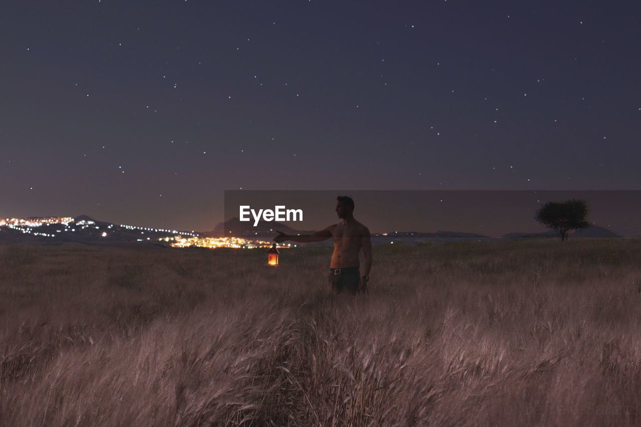 Shirtless man with illuminated lantern standing on field