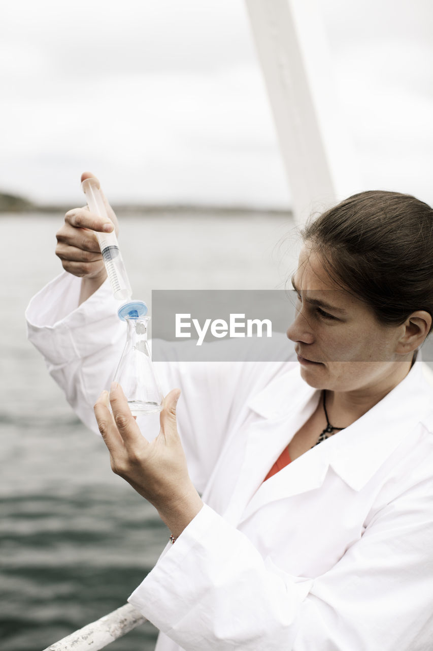 Female scientist injecting water in flask on boat in sea