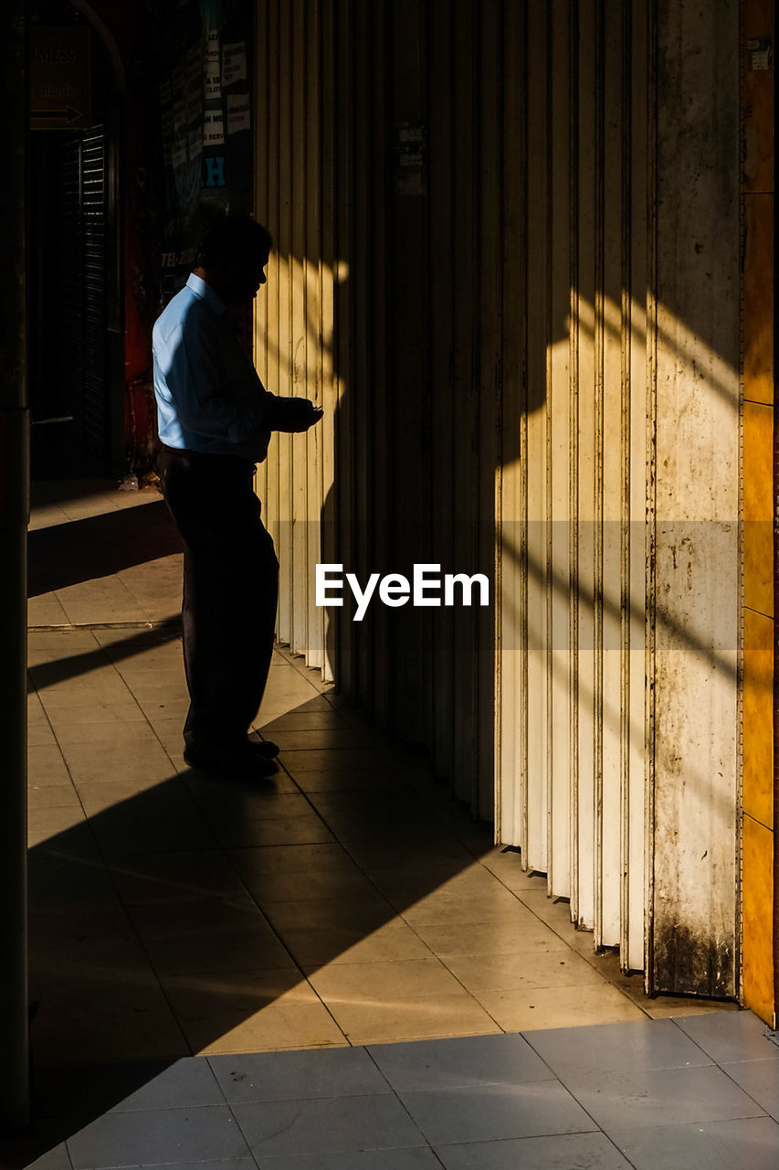 REAR VIEW OF SILHOUETTE MAN STANDING ON TILED FLOOR